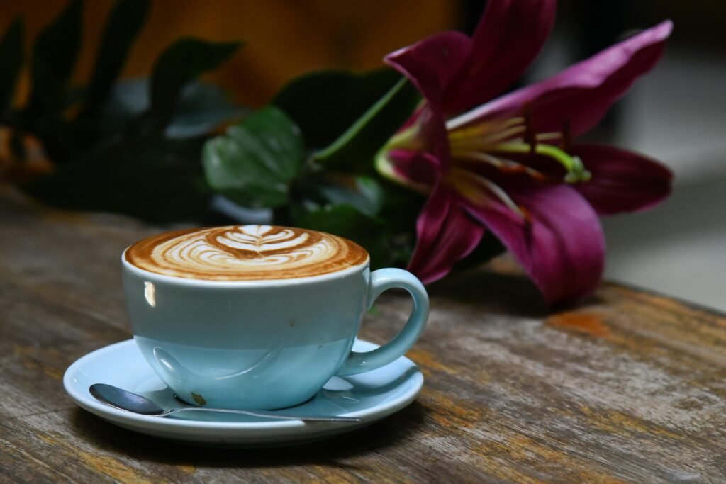 pexels photo 34184241 34184241 A beautifully crafted latte with intricate art beside a vibrant purple lily on a rustic wooden table.