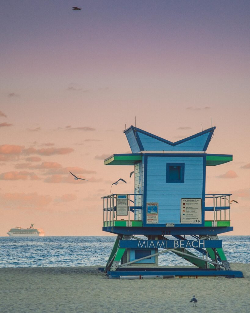A tranquil scene of Miami Beach at sunset featuring a colorful lifeguard tower and a serene ocean view.